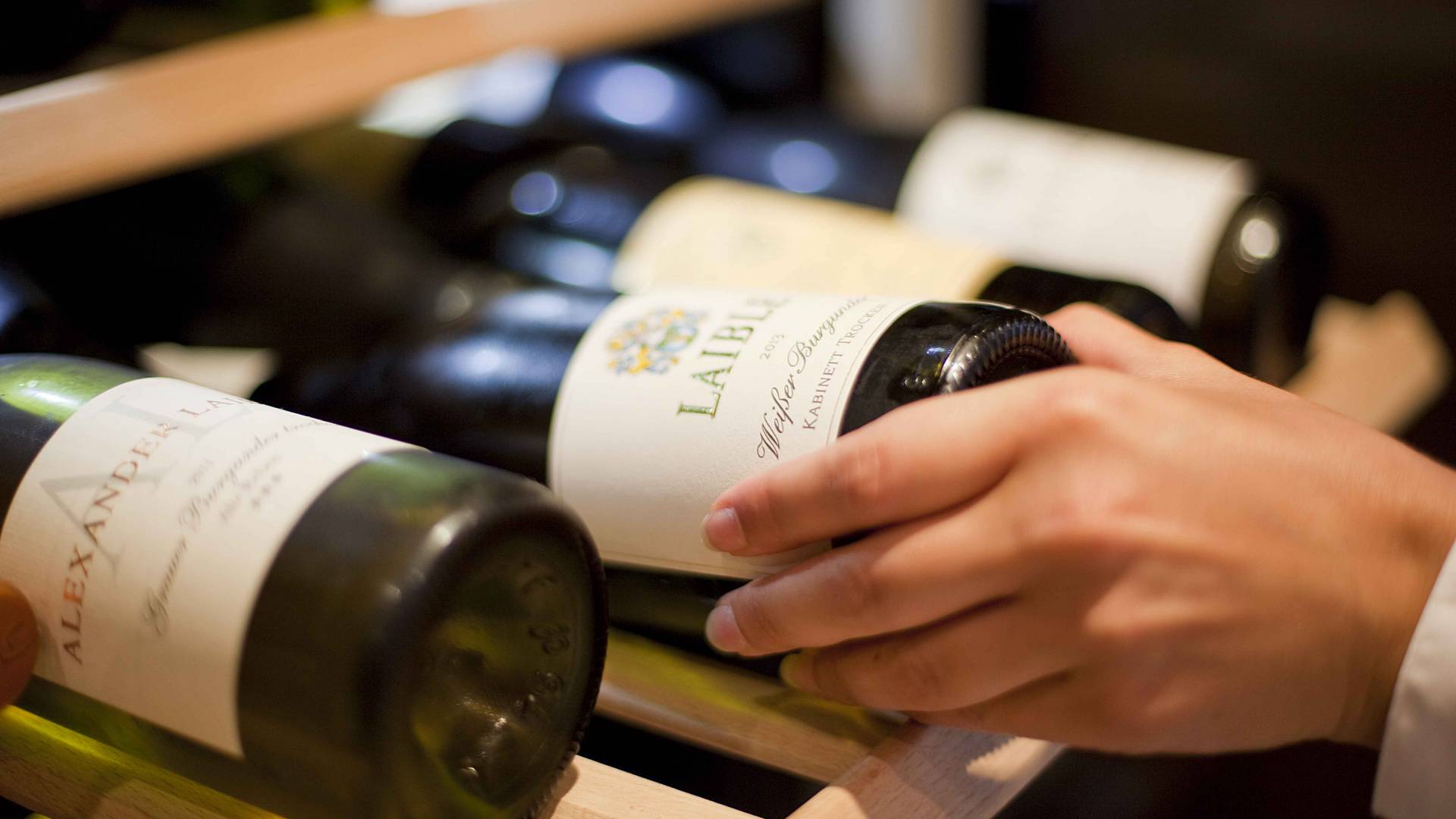 Frau nimmt eine Rotwein Flasche aus dem Weinschrank